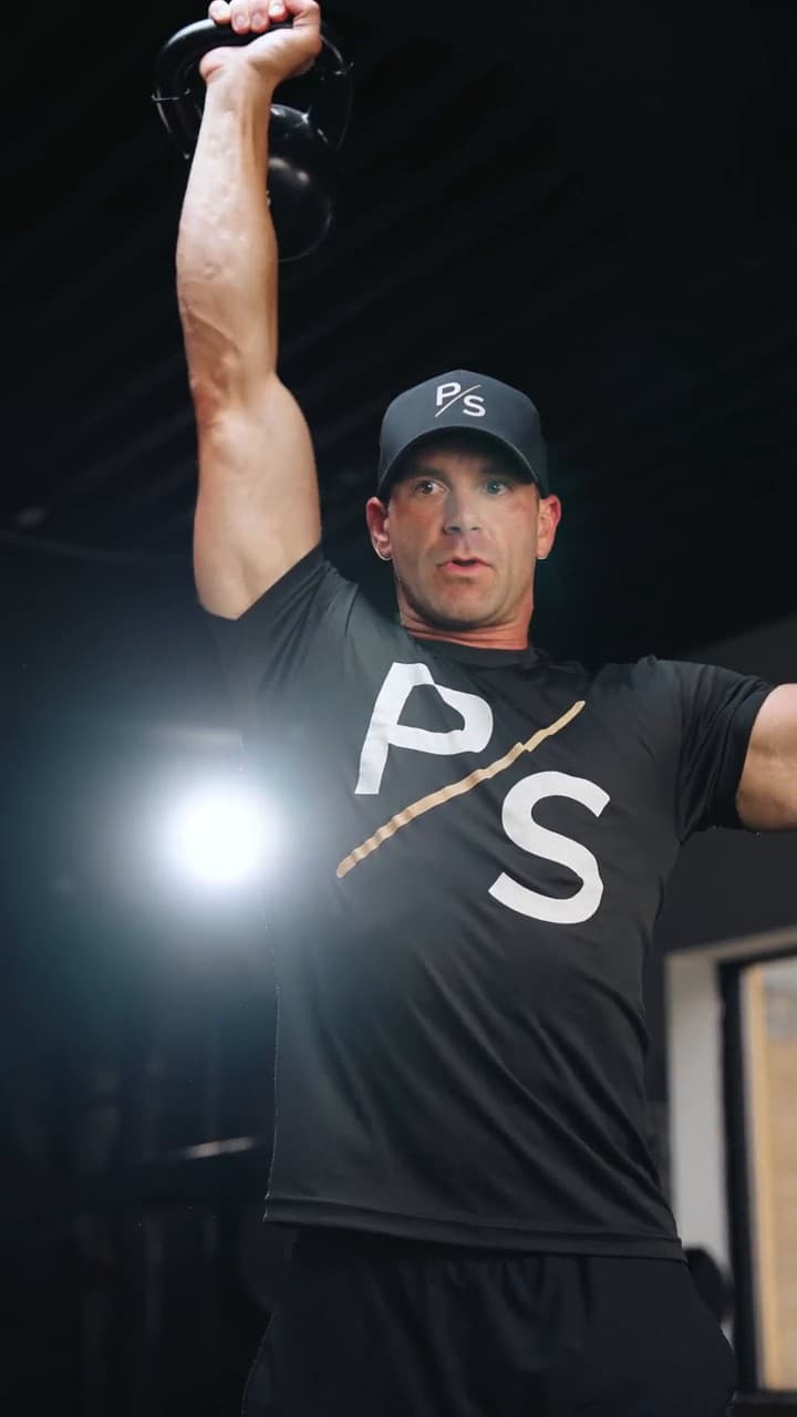 Chris Karagitsis pressing a kettlebell overhead in a Pure Strike shirt